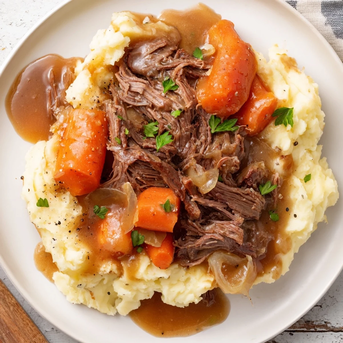 Fork-tender Slow Cooker Pot Roast served on a bed of fluffy, buttery mashed potatoes, a classic dinner.