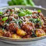 Savory Sausage Gnocchi with Kale served hot in a skillet, featuring wilted greens and spicy Italian sausage crumbles.