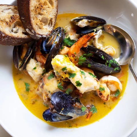 A steaming bowl of bouillabaisse, filled with delicious seafood and vegetables, looks inviting.