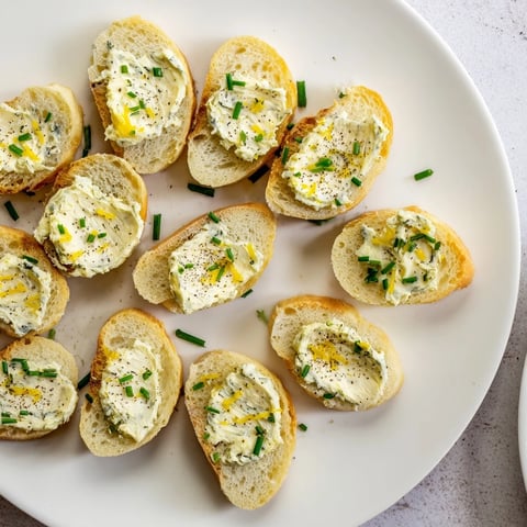 Golden-brown vodka butter crostini spread on a baking sheet, with lemon zest and chives garnish.