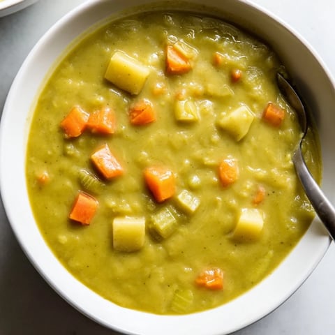 Creamy split pea soup simmering in a rustic pot, with diced carrots and potatoes in a smoky, steamy broth.
