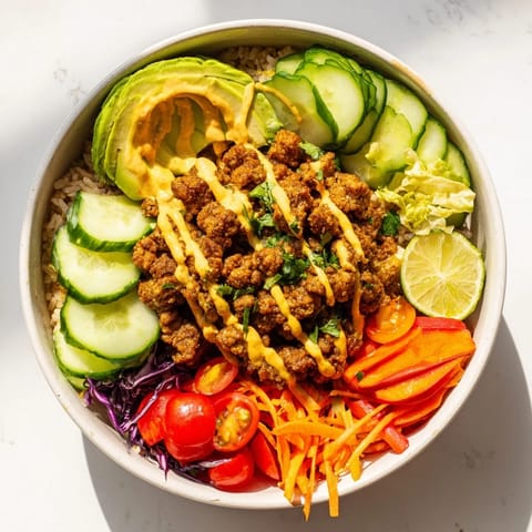 Delicious plant-based meat bowl featuring vibrant veggies and spicy mayo drizzle.  