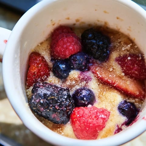 A close-up of a warm mixed berry cobbler mug cake, a quick sweet treat for any craving.