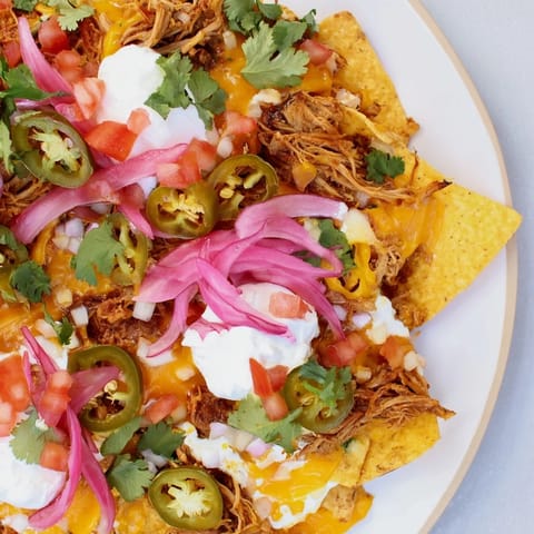 Golden, baked loaded nachos with pulled pork, featuring melty queso, spicy jalapeños, and fresh toppings.