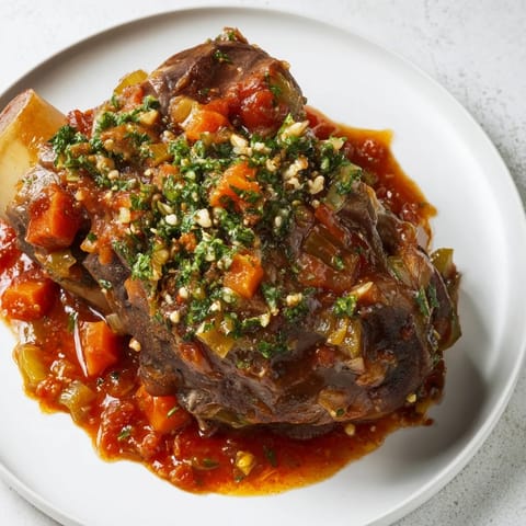 Golden-brown, slow-braised Osso Buco served with a vibrant gremolata, perfect for a cozy dinner.