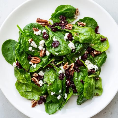 A close-up of the spinach goat cheese salad featuring crumbled cheese, sweet cranberries, and crunchy candied pecans glistening with tangy dressing.  