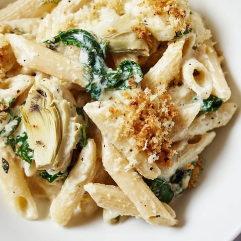 A close-up of a freshly baked Artichoke Pasta Bake, showcasing melted cheese, crispy breadcrumbs, and tender artichoke hearts nestled among penne pasta.