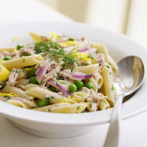 A close-up of Lemony Tuna Pasta Salad with fork-twisted fusilli, bright lemon zest, diced red onion, and juicy cherry tomatoes, perfect for a summer picnic spread.  
