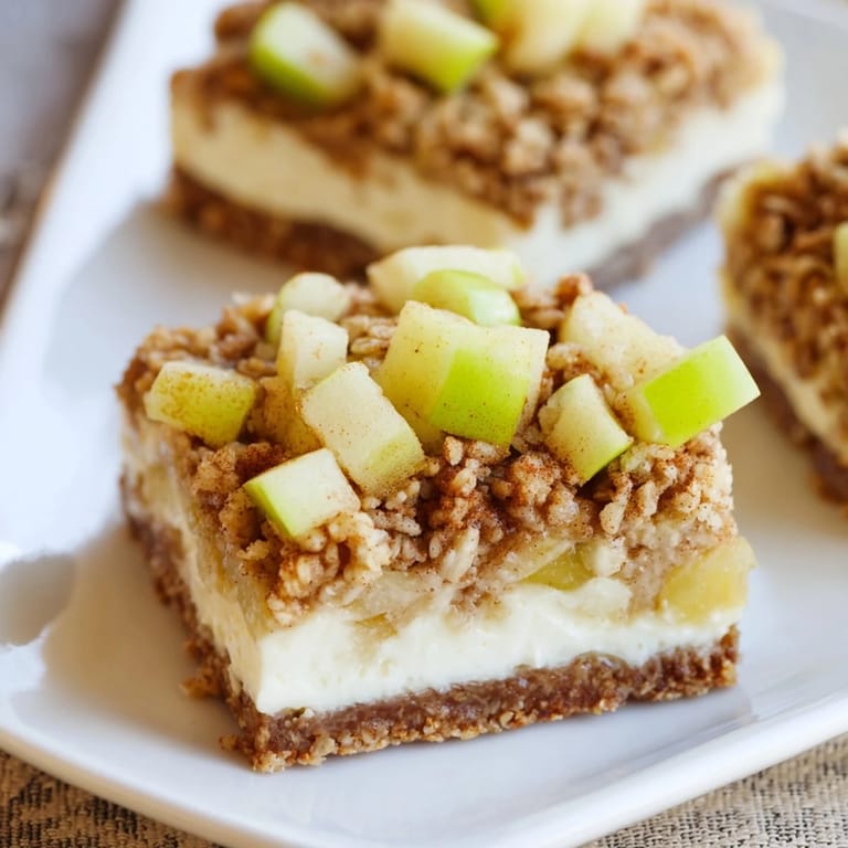 A close-up of baked Apple Crisp Cheesecake Bars, showing layers of apple, cream cheese, and oat crisp.