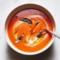 A warm bowl of Tomato and Basil Soup, garnished with fresh basil leaves and a drizzle of olive oil beside crusty bread.  